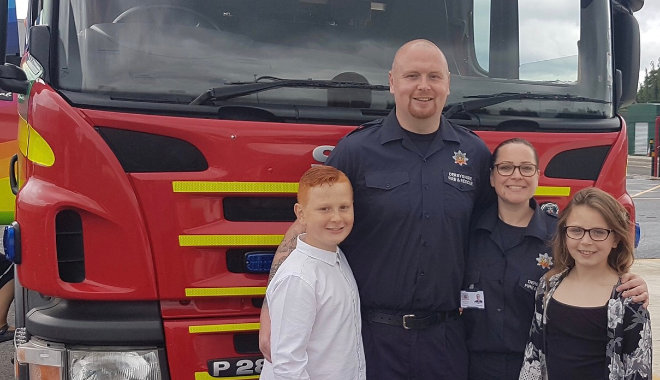 bev with husband both in on-call kit stood in front of fire engine along with their son and daughter